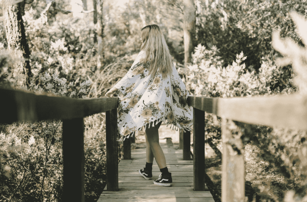 Hippie girl with long blond hair walking across a bridge into a forest
