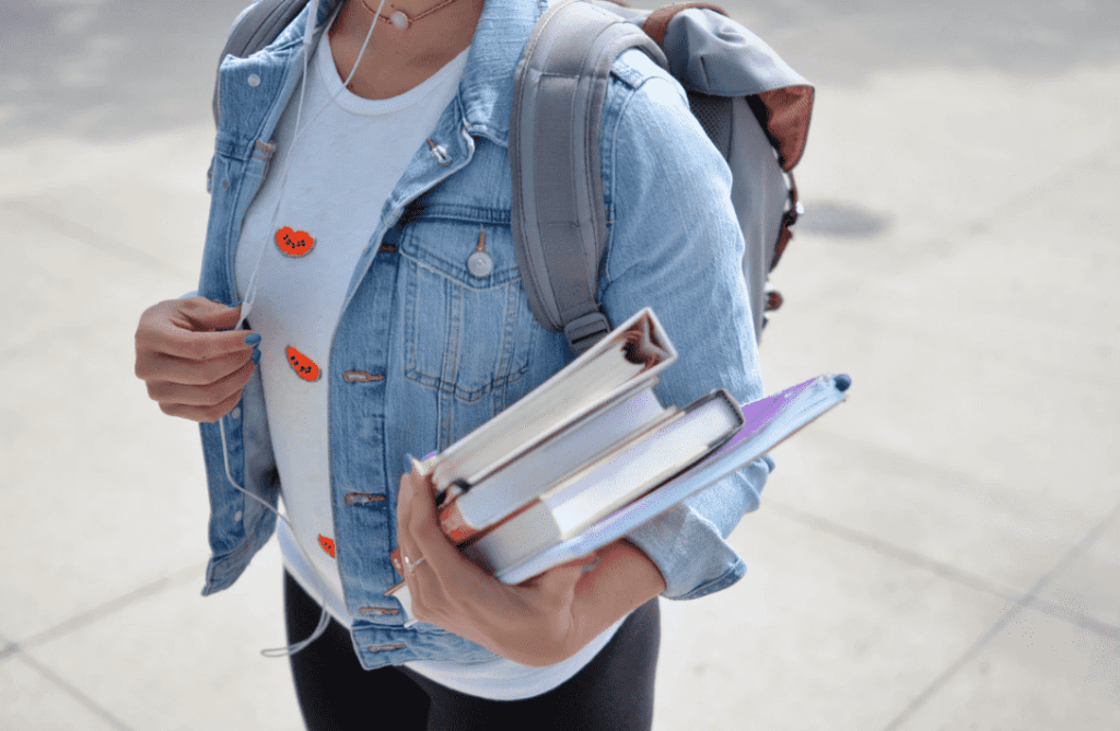 Student wearing backpack holding university books and listening to music